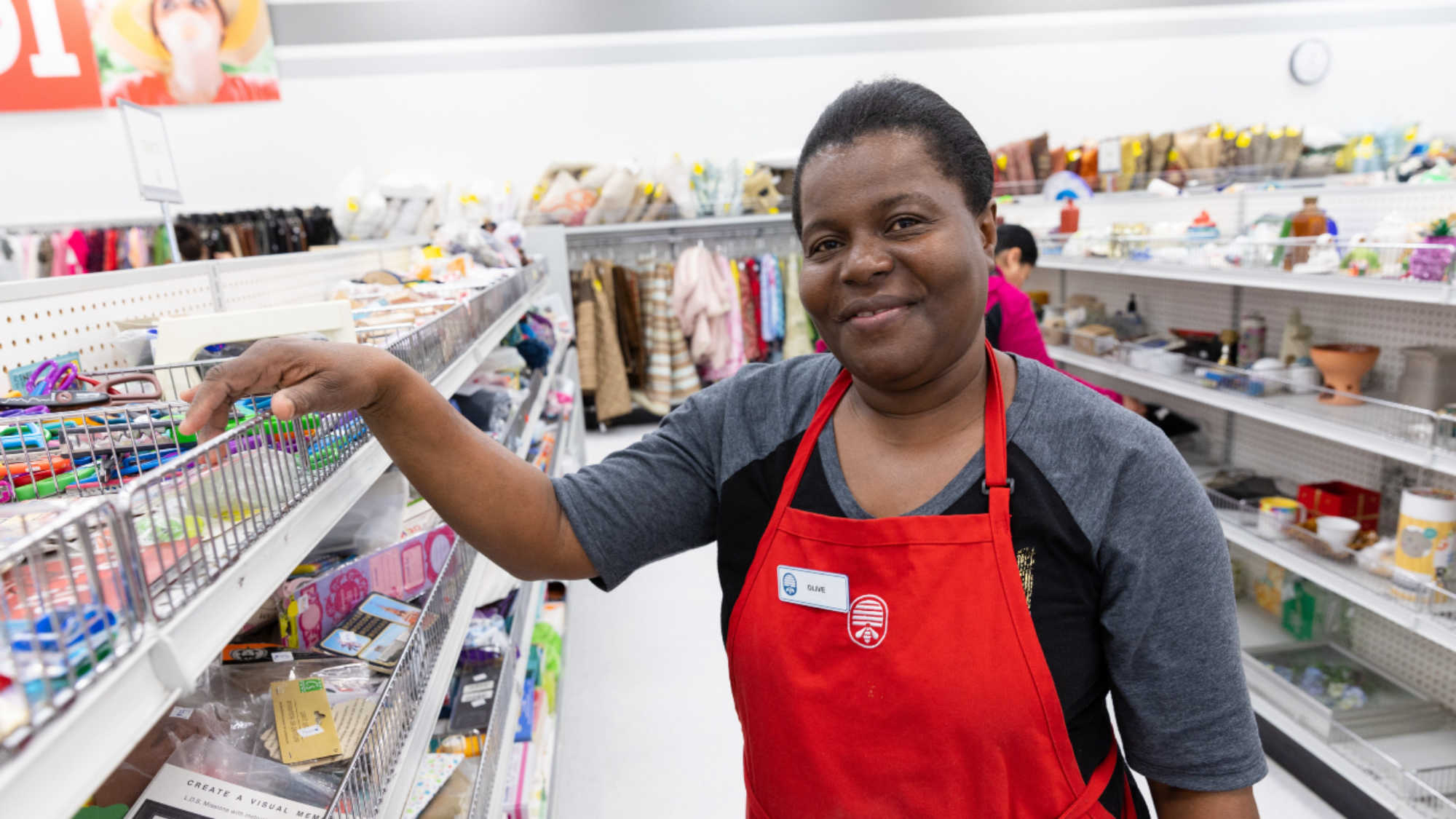 A female DI associate smiles next to the store shelves she has been organizing.